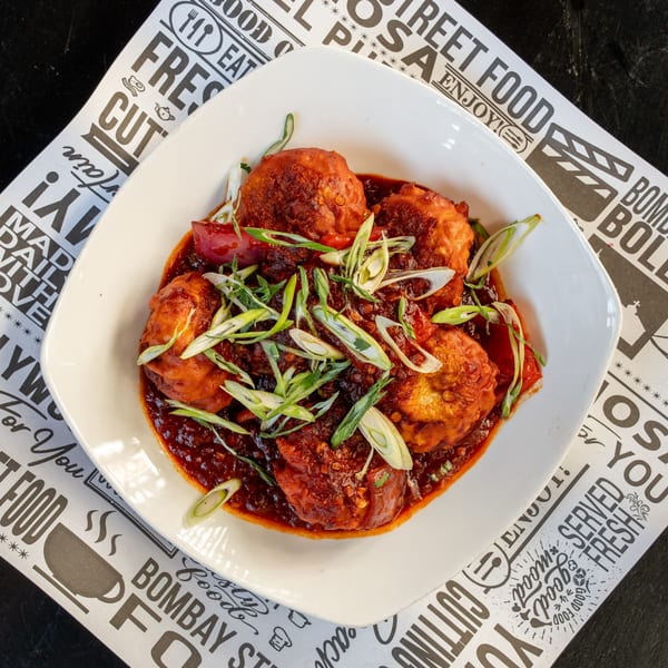 Bombay Street Food's Indian dish, Manchurian Momos, in a white bowl on a branded paper liner.