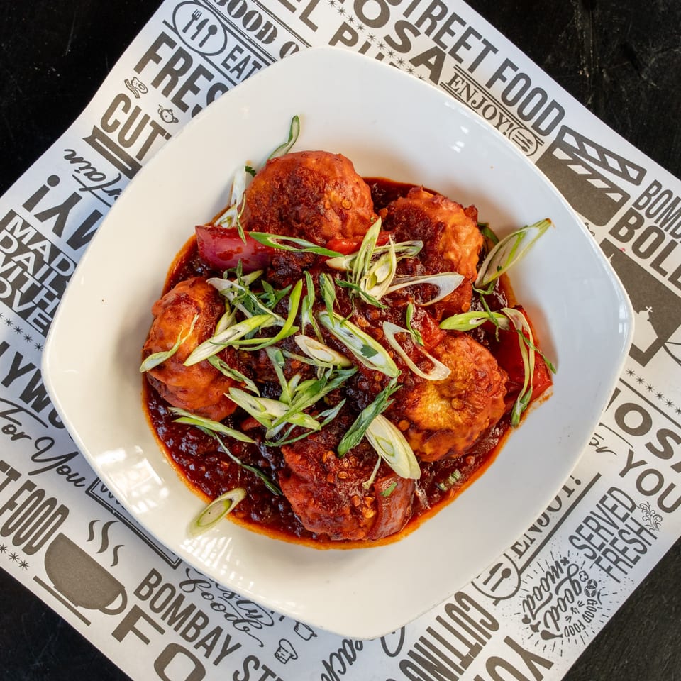 Bombay Street Food's Indian dish, Manchurian Momos, in a white bowl on a branded paper liner.