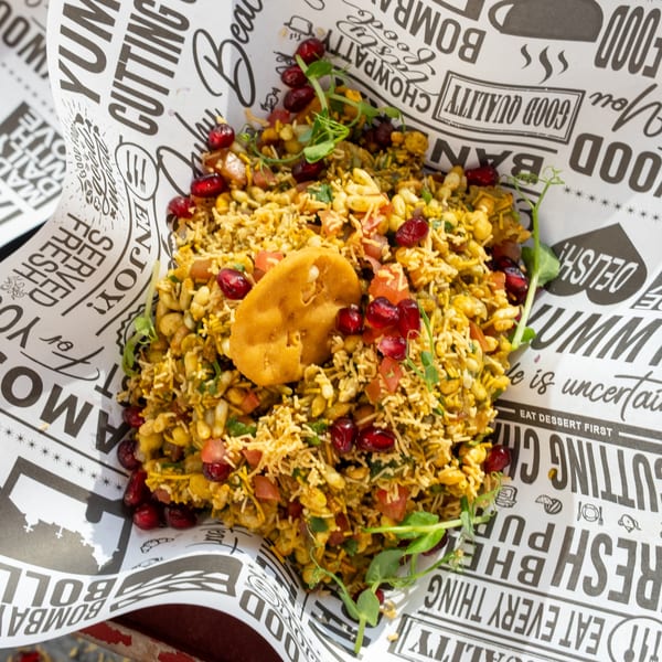 Indian Bhel Puri street food, garnished with pomegranate seeds and a fried pastry, served in paper.