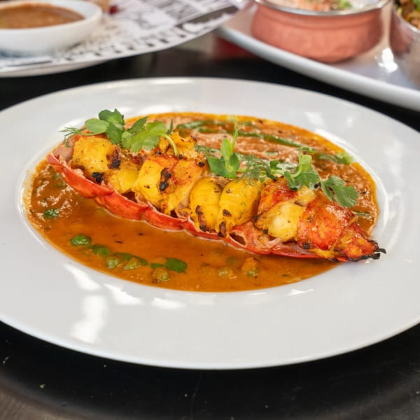 Grilled lobster tail in a rich orange curry sauce, garnished with fresh herbs on a white plate.
