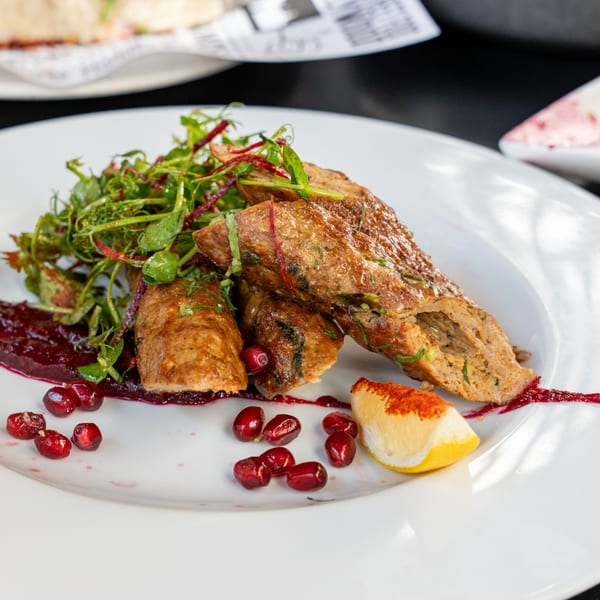 Indian seekh kebabs with fresh greens, pomegranate seeds, and a lemon wedge on a white plate.