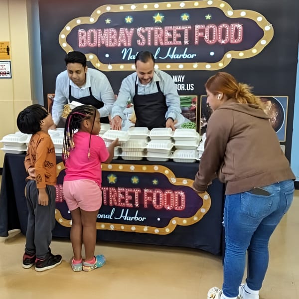 Bombay Street Food staff serving takeout containers to a woman and two children at a food stall.
