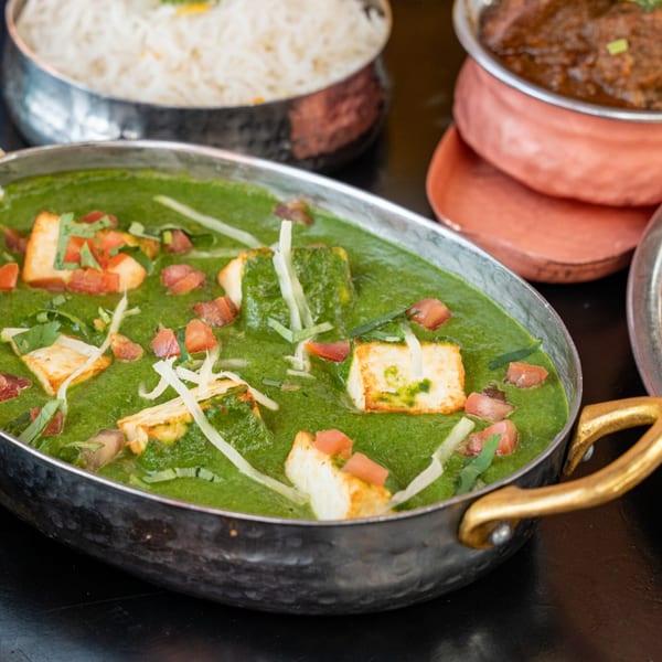 Palak Paneer, a vibrant green Indian spinach and cheese dish, garnished with tomatoes and shredded cheese.