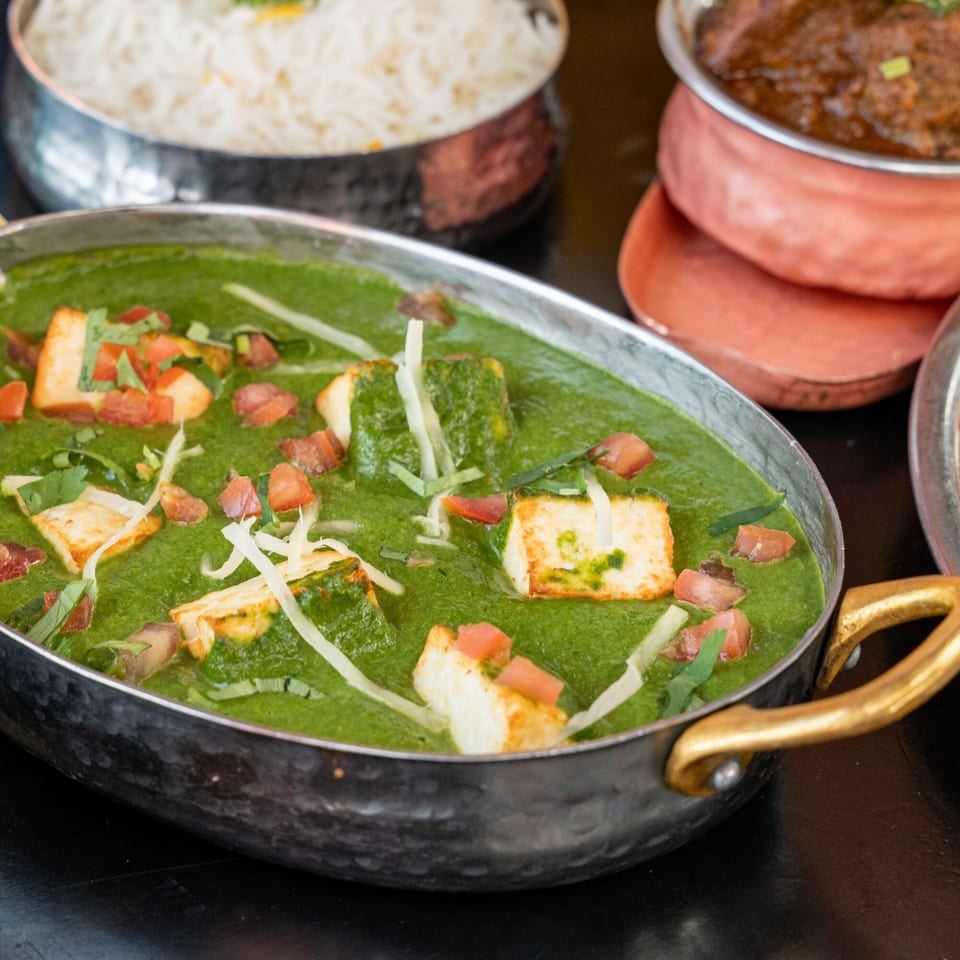 Palak Paneer, a vibrant green Indian spinach and cheese dish, garnished with tomatoes and shredded cheese.