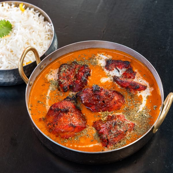 A metal bowl of Bombay Street Food's Chicken Tikka Masala with a side of white rice.
