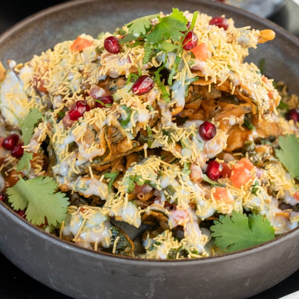 A close-up of Bombay Street Food's Indian chaat, topped with yogurt, pomegranate, cilantro, and crispy sev.